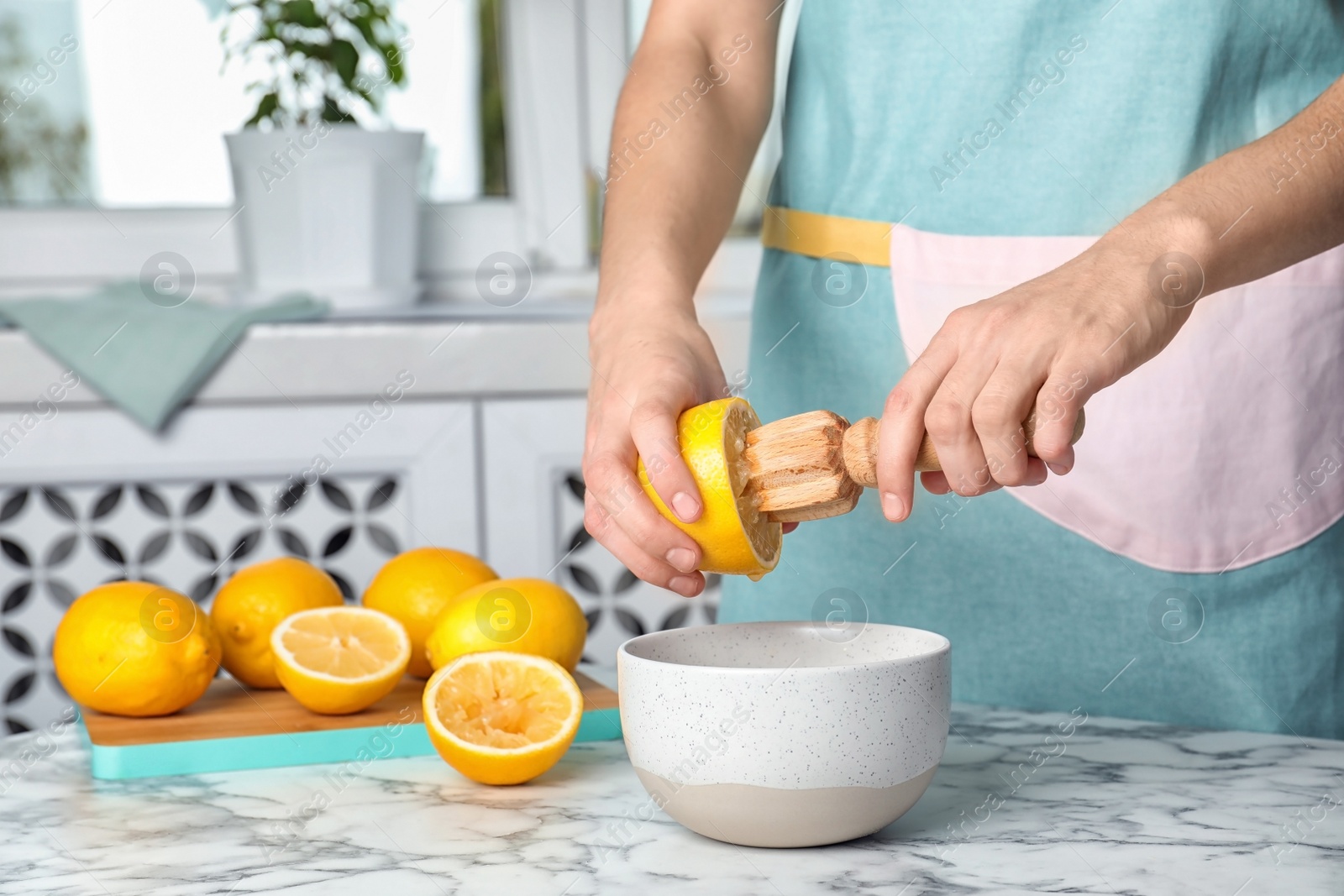 Photo of Woman squeezing fresh lemon juice with wooden reamer into bowl on table