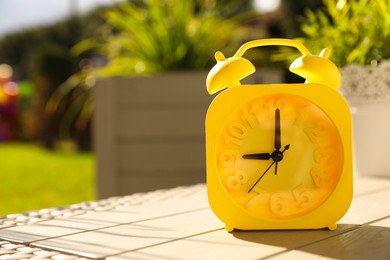 Photo of Yellow alarm clock on white wooden table outdoors at sunny morning. Space for text