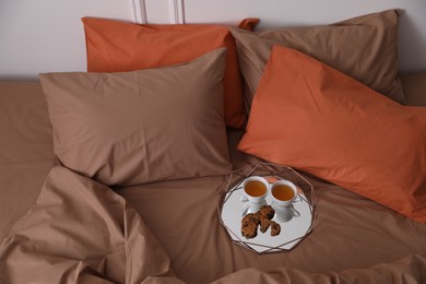 Cups of hot drink and cookies on bed with brown linens in stylish room, above view