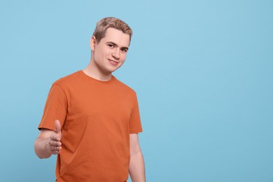 Photo of Happy man inviting to come in against light blue background, space for text