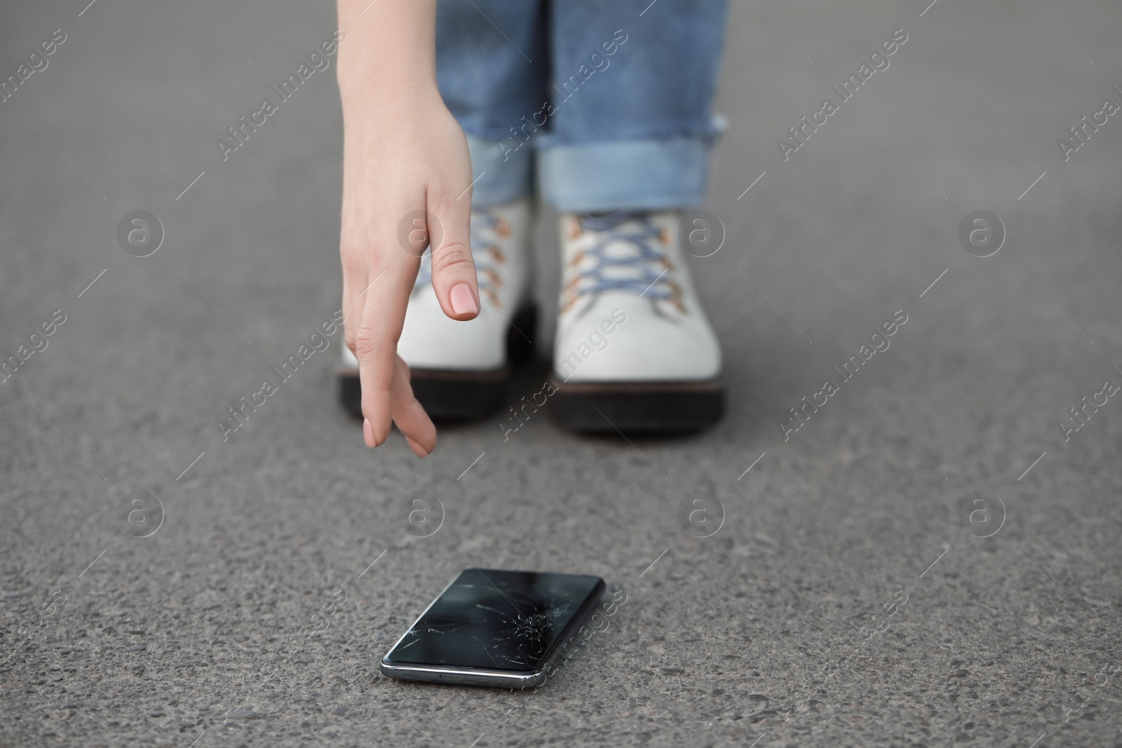 Photo of Woman taking dropped smartphone from asphalt, closeup. Device repairing