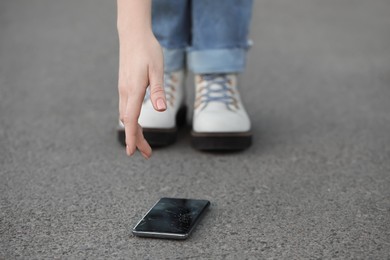 Photo of Woman taking dropped smartphone from asphalt, closeup. Device repairing