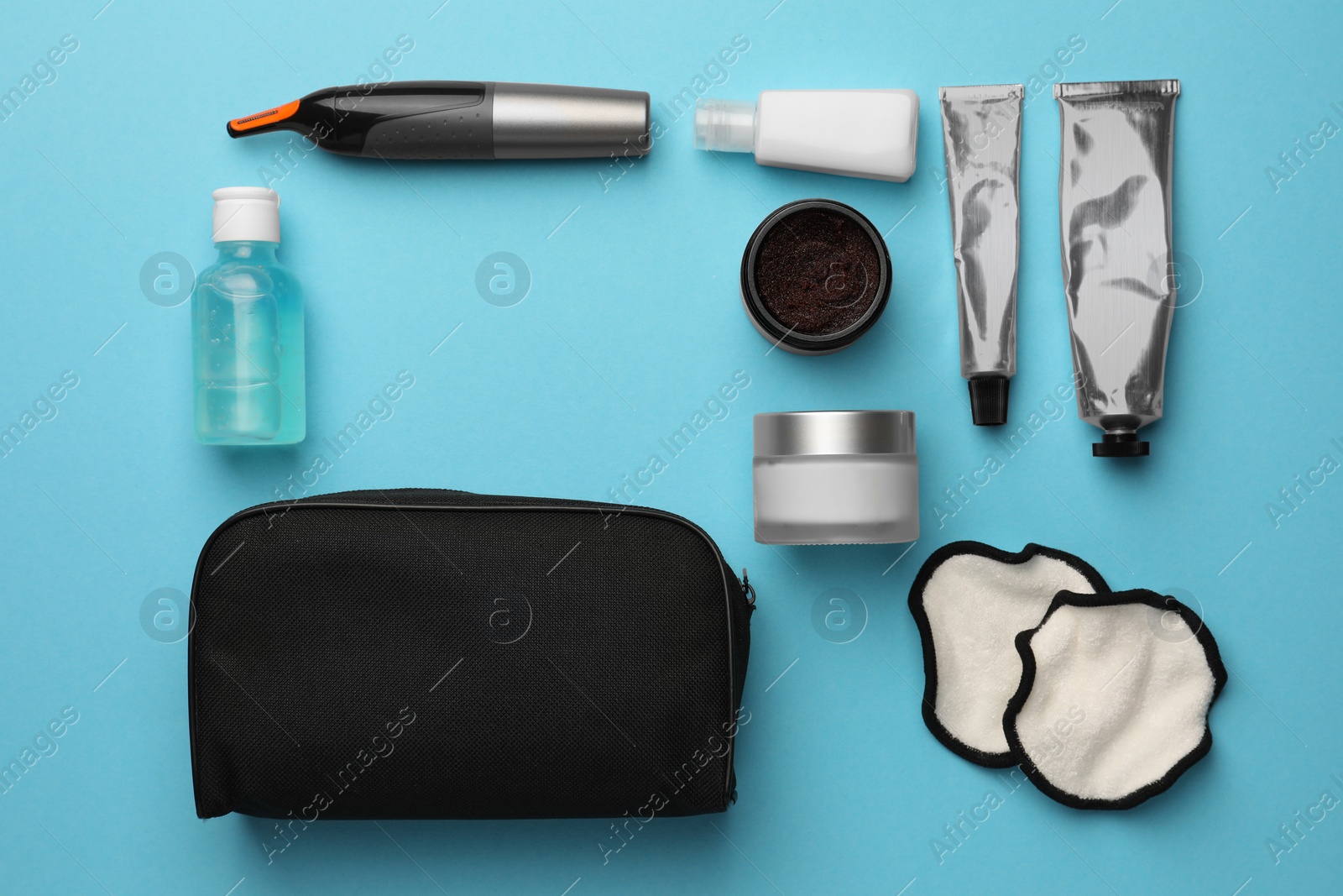 Photo of Preparation for spa. Compact toiletry bag with different cosmetic products on light blue background, flat lay