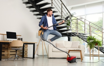 Photo of Young man having fun while vacuuming in living room