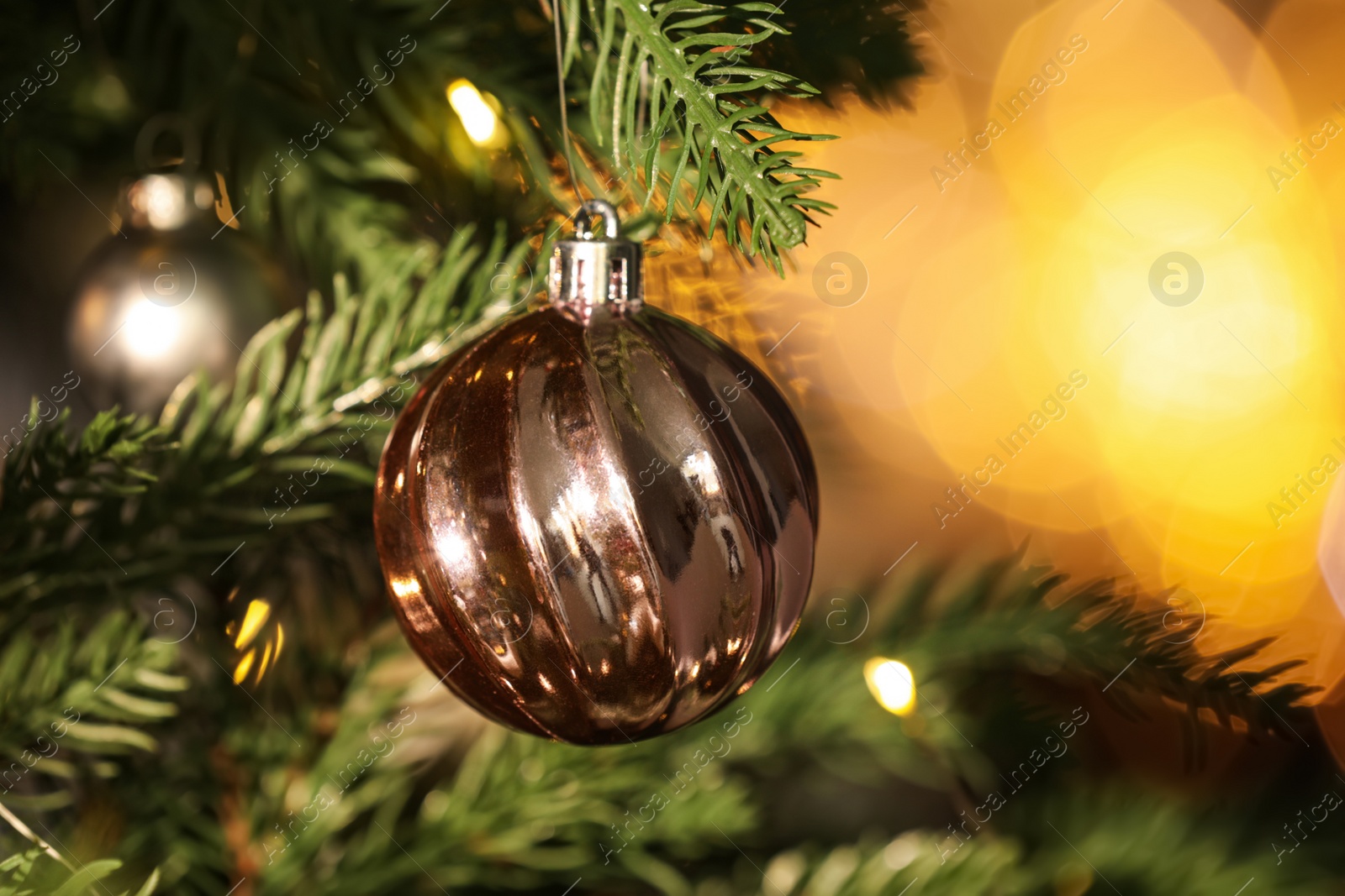 Photo of Beautiful shiny holiday bauble hanging on Christmas tree against blurred fairy lights, closeup. Space for text