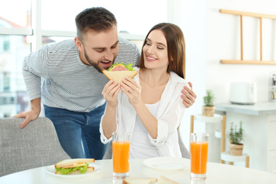 Photo of Happy couple having breakfast with sandwiches at table in kitchen