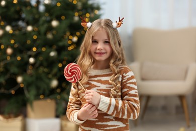 Photo of Portrait of cute girl with lollipop near Christmas tree at home