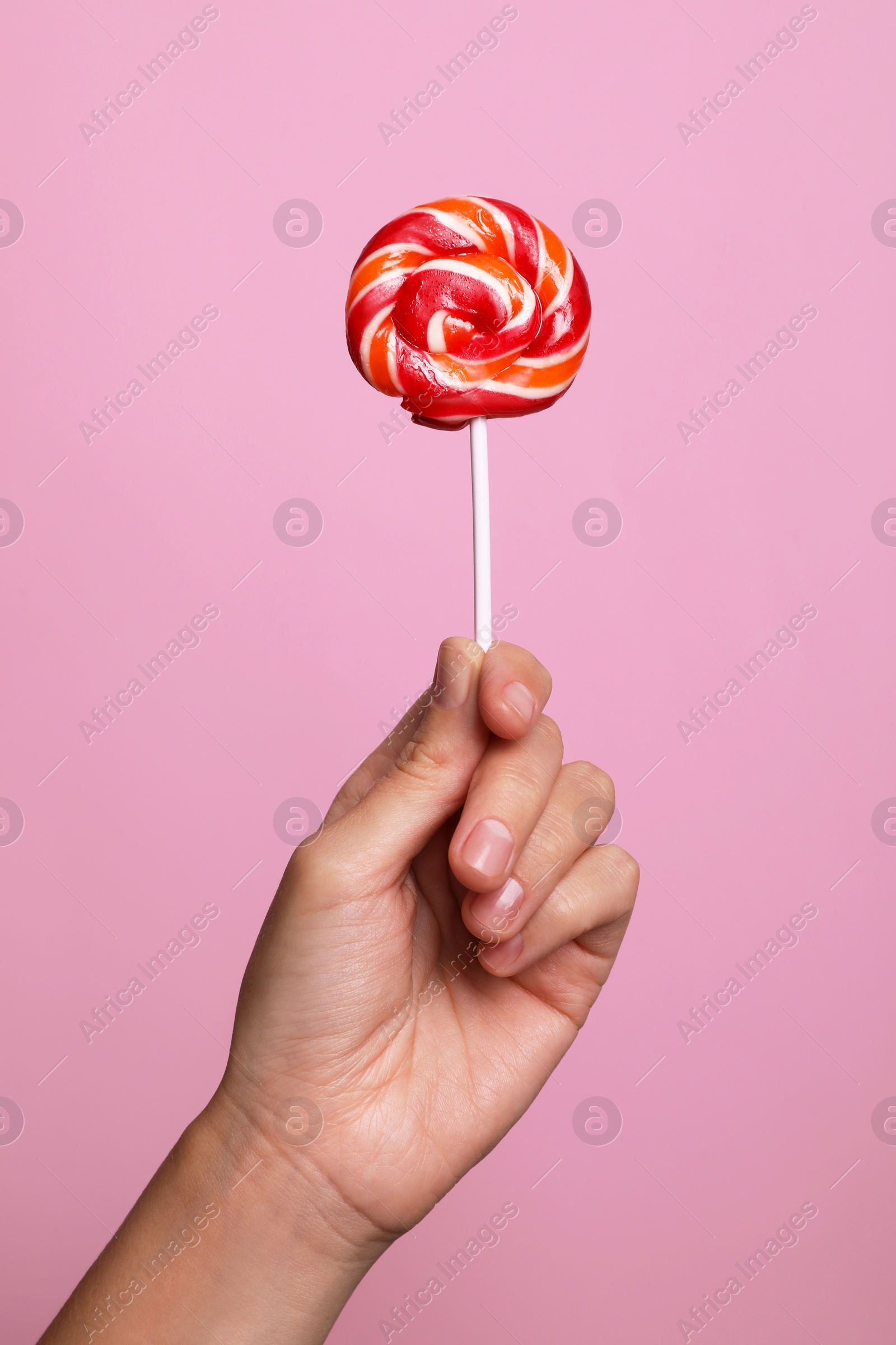 Photo of Woman holding bright tasty lollipop on pink background, closeup