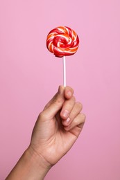 Woman holding bright tasty lollipop on pink background, closeup