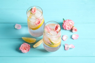 Photo of Tasty refreshing lemon drink with roses on light blue wooden table