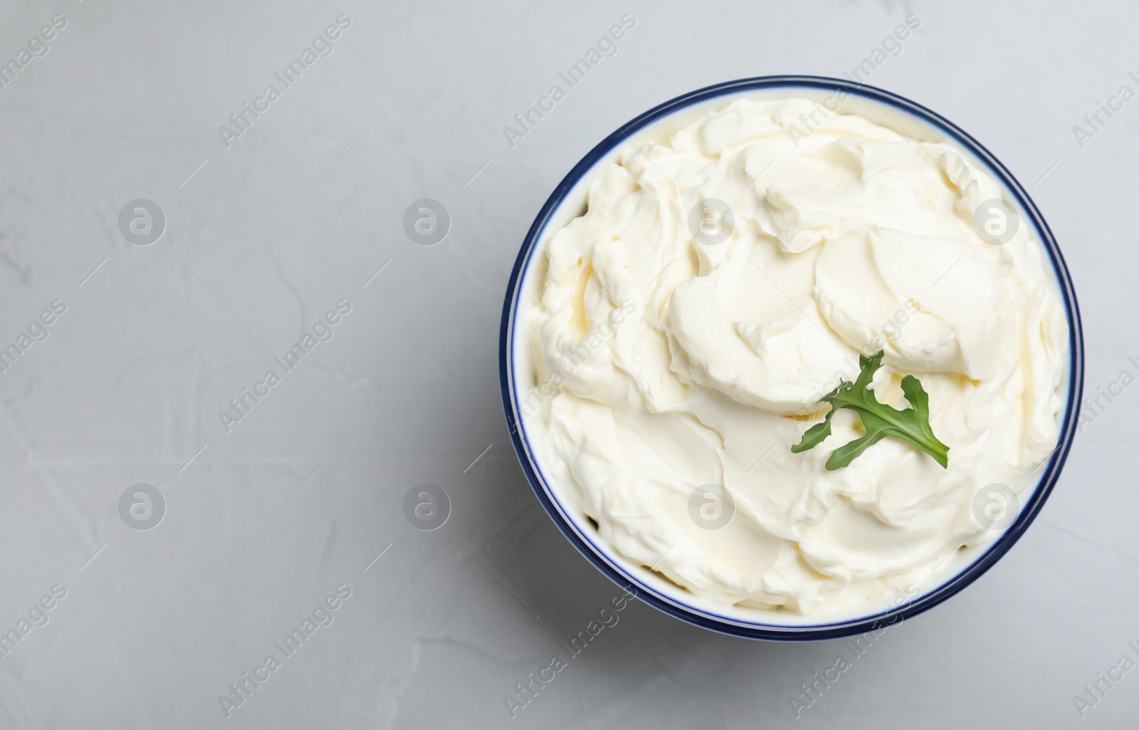Photo of Bowl of tasty cream cheese and arugula on grey table, top view. Space for text
