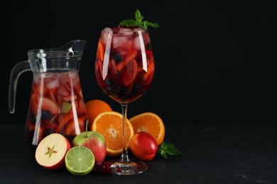 Glass and jug of Red Sangria with fruits on black table, space for text
