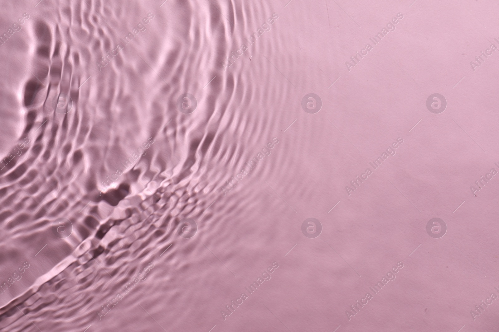 Photo of Rippled surface of clear water on pink background, top view