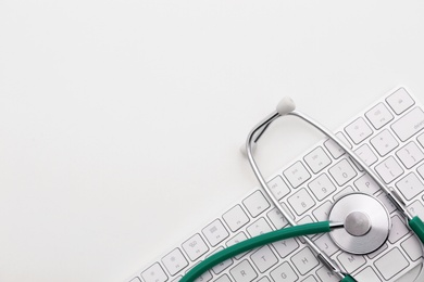 Photo of Modern keyboard and stethoscope on light background, space for text. Technical support concept