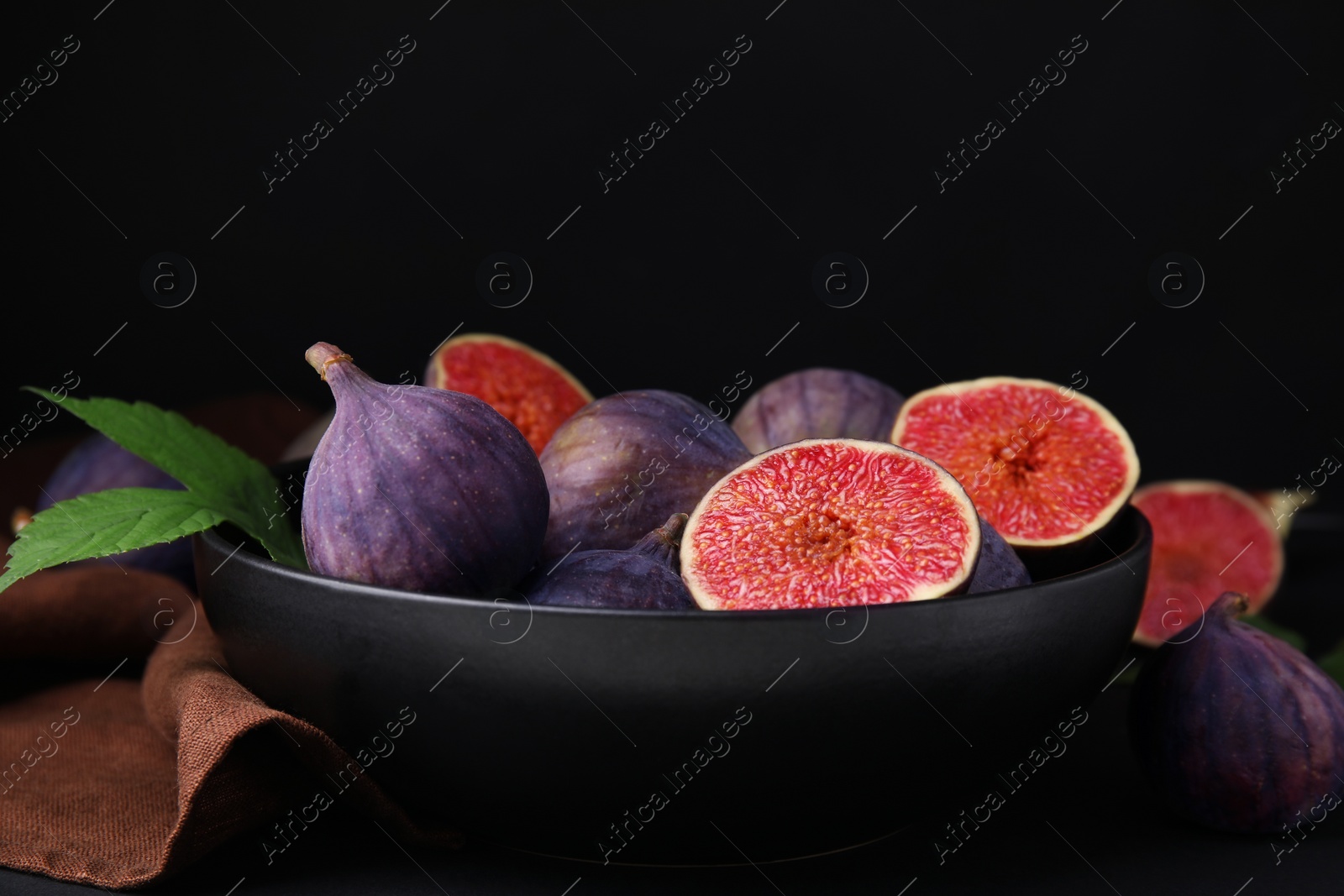 Photo of Bowl with fresh ripe purple figs on black table
