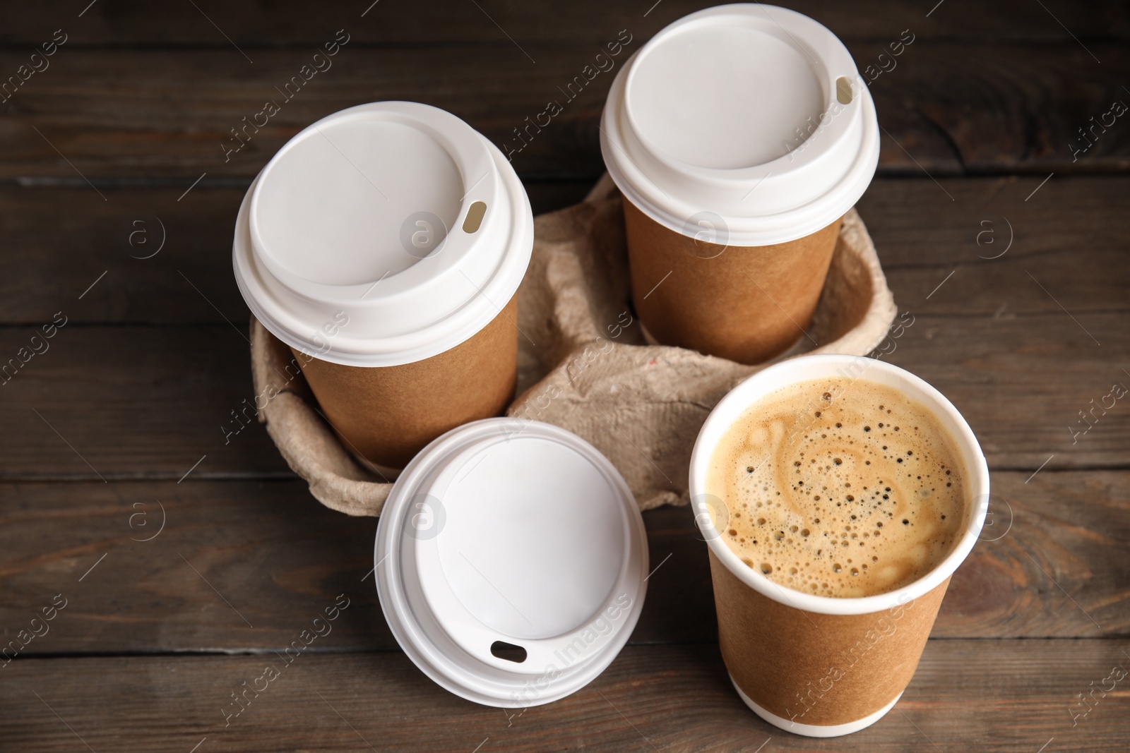 Photo of Takeaway paper coffee cups with plastic lids and cardboard holder on wooden table