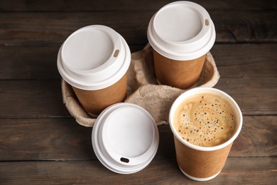 Photo of Takeaway paper coffee cups with plastic lids and cardboard holder on wooden table