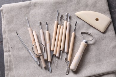 Photo of Set of different clay crafting tools on grey fabric, top view