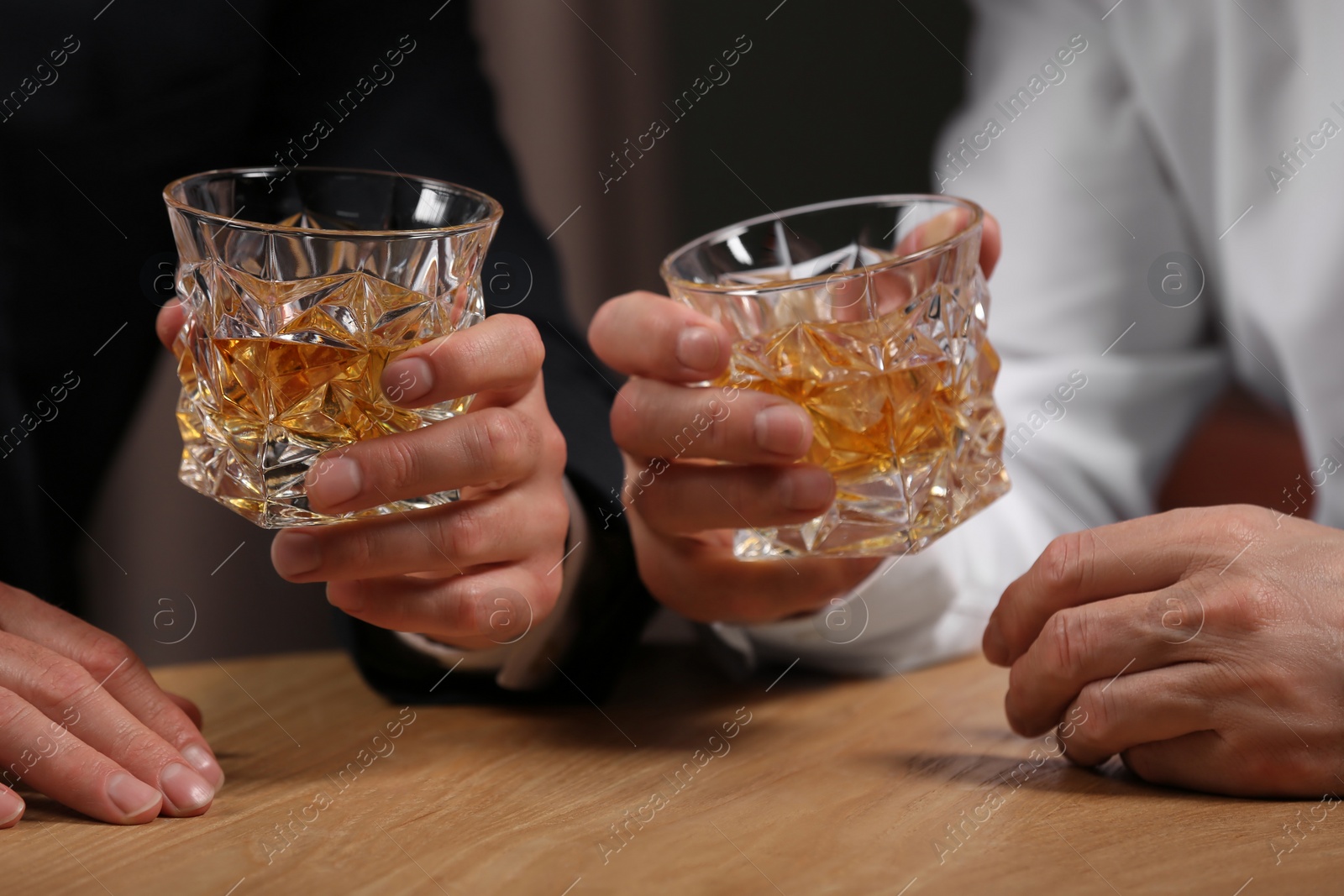 Photo of Men with glasses of whiskey at wooden table indoors, closeup