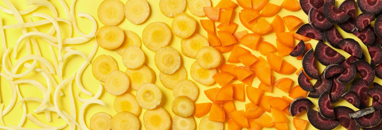 Photo of Pieces of raw color carrots on yellow background, flat lay