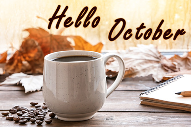 Image of Hello October card. Cup of hot drink and autumn leaves on wooden table