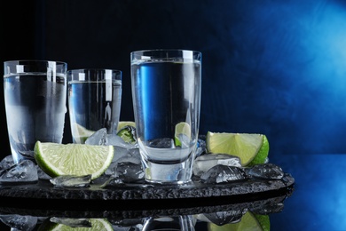 Photo of Vodka in shot glasses and lime slices on dark background with blue light