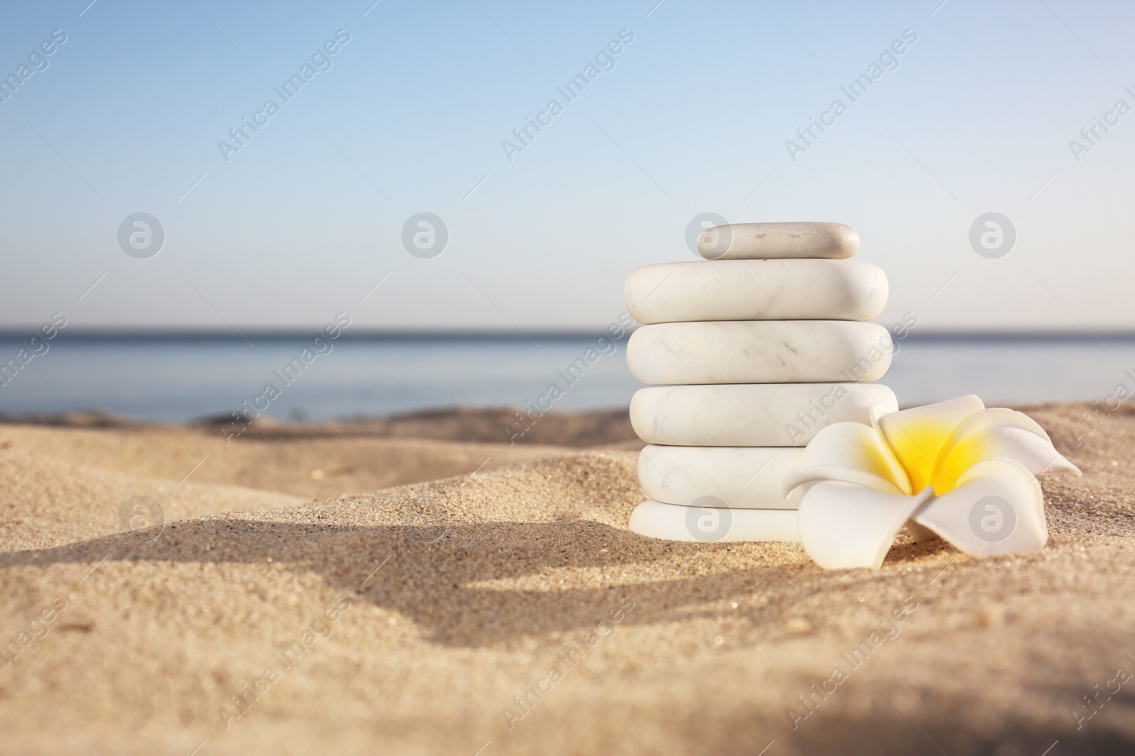 Photo of Stack of white marble stones and beautiful flower on sandy beach near sea, space for text. Zen concept