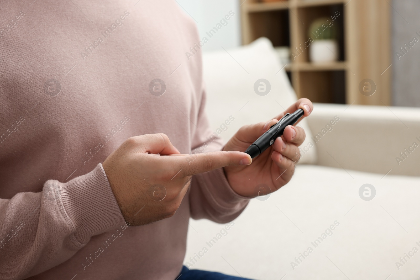 Photo of Diabetes test. Man checking blood sugar level with lancet pen at home, closeup