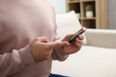 Photo of Diabetes test. Man checking blood sugar level with lancet pen at home, closeup