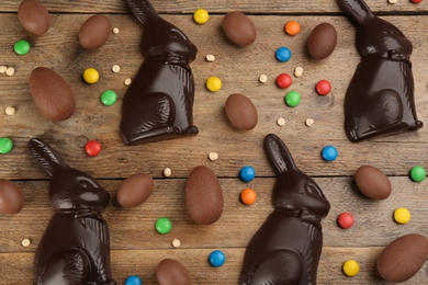 Photo of Dark chocolate Easter bunnies, candies and eggs on wooden table, flat lay