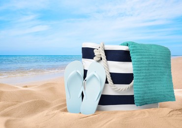 Stylish bag with different accessories on sandy beach near ocean