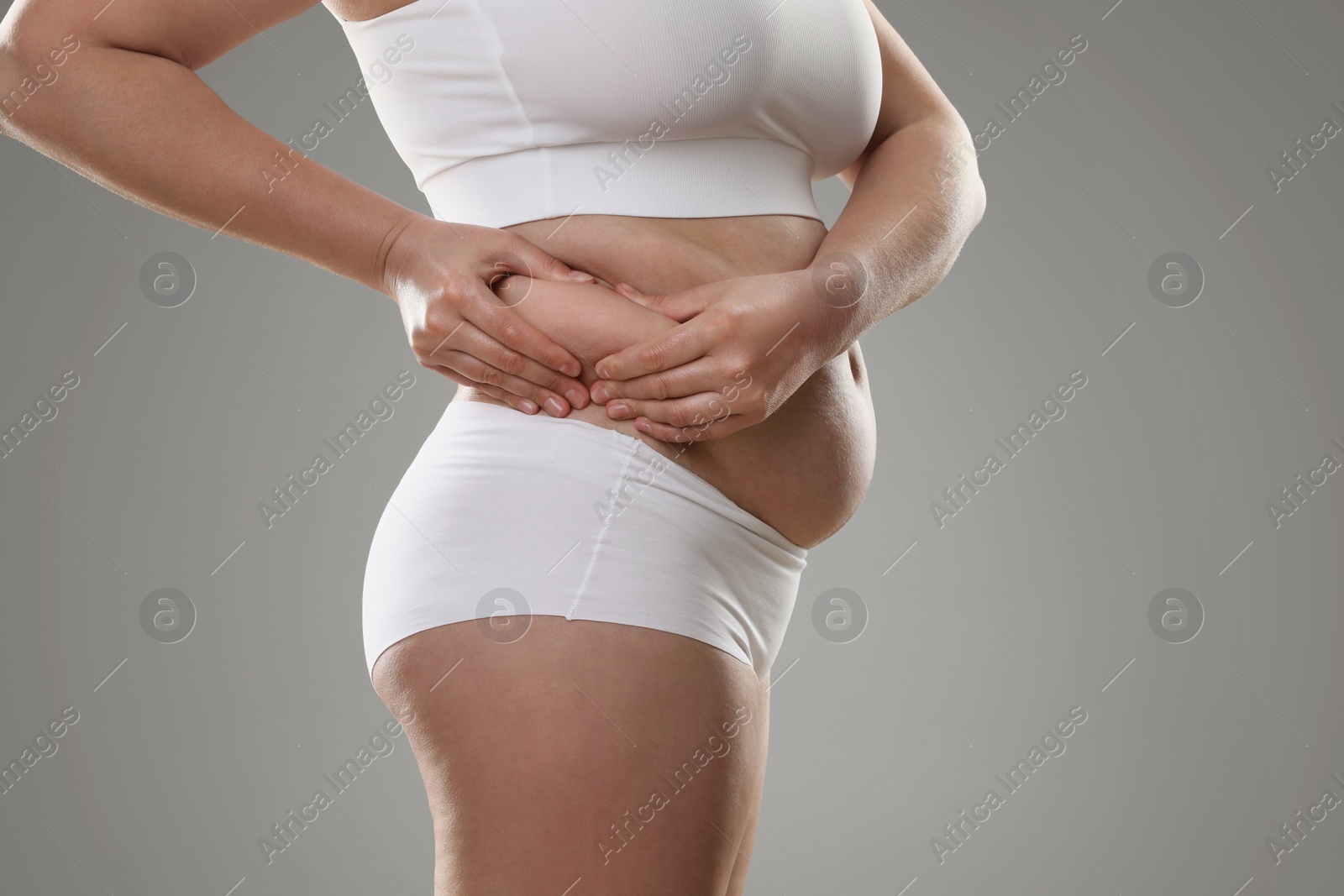 Photo of Woman touching belly fat on grey background, closeup. Overweight problem