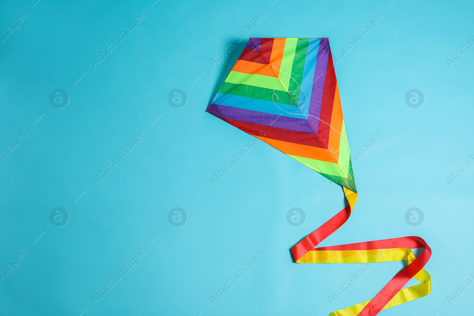 Photo of Bright rainbow kite on light blue background, top view. Space for text