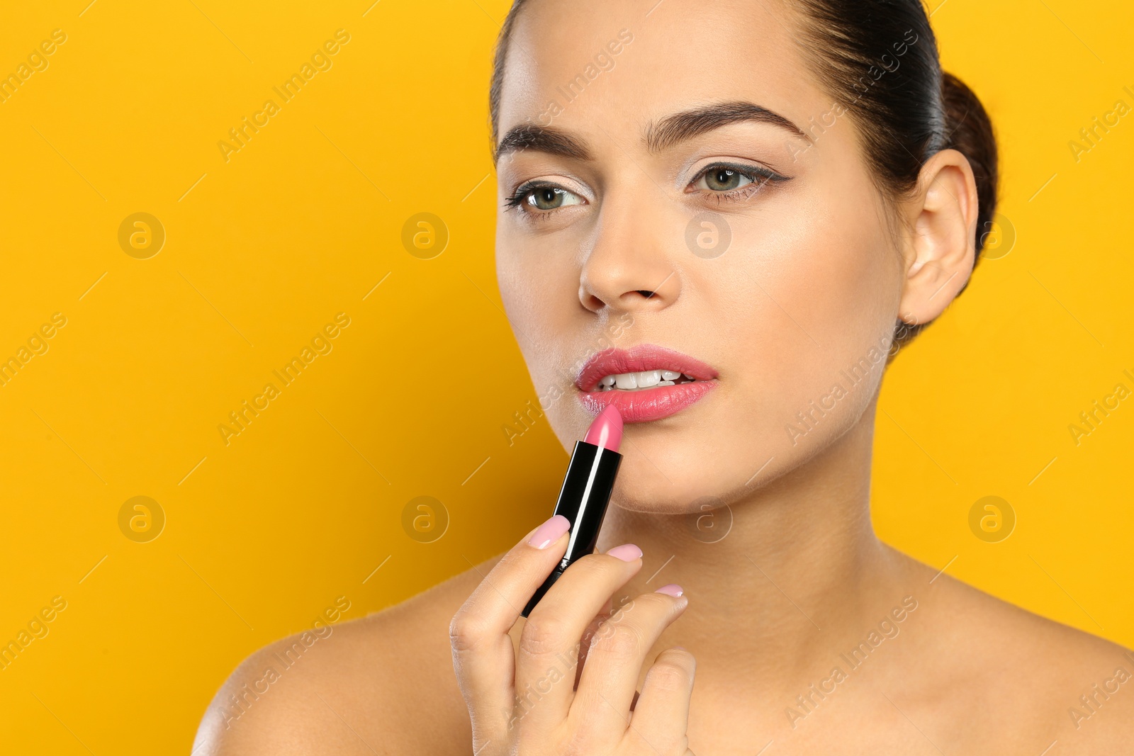 Photo of Young woman applying lipstick on color background