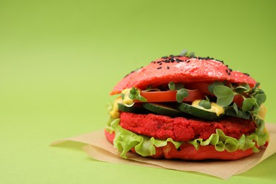 Photo of Tasty pink vegan burger with vegetables, patty and microgreens on light green background, closeup. Space for text