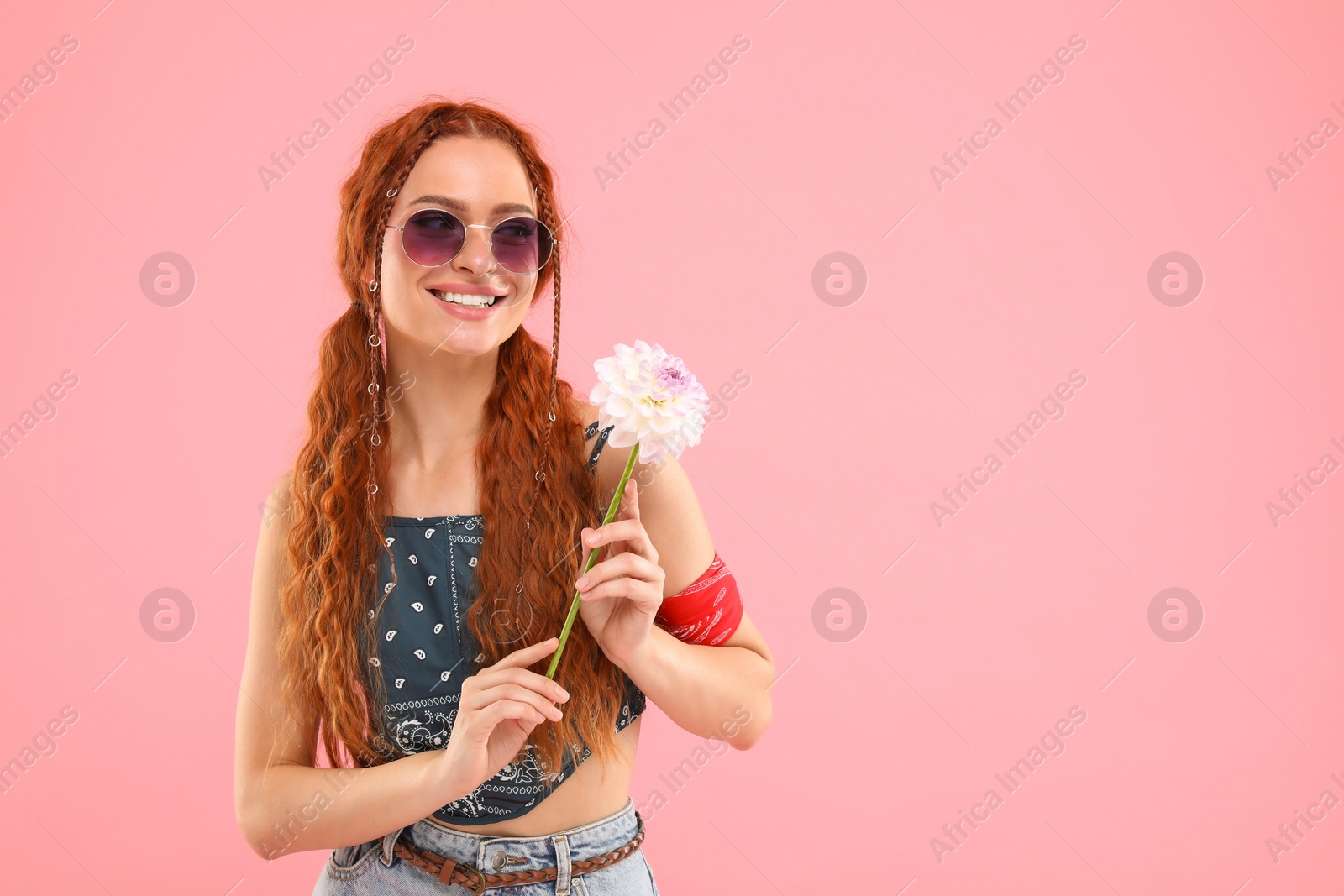 Photo of Stylish young hippie woman with dahlia flower on pink background, space for text