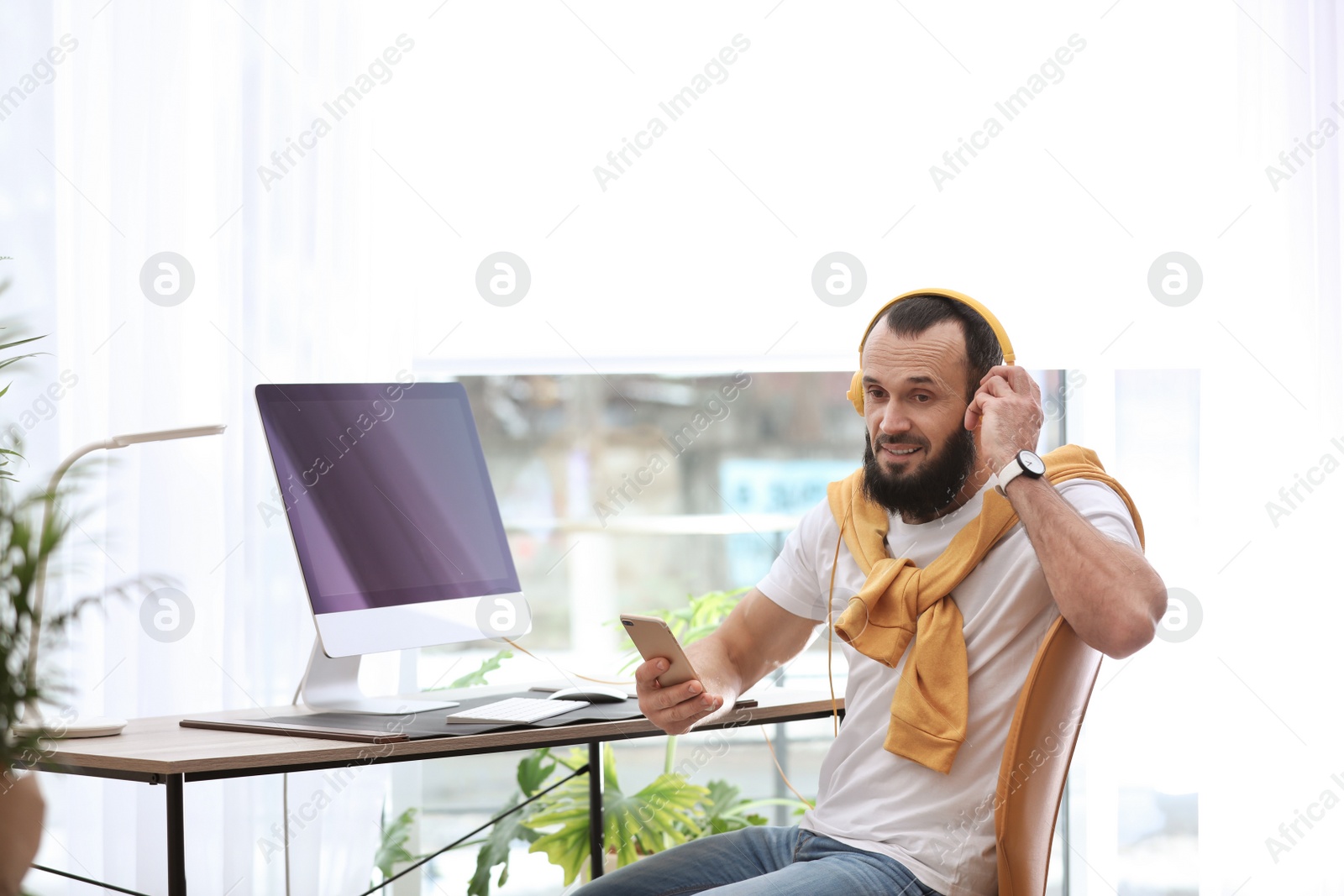 Photo of Mature man with headphones and computer in home office