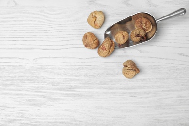 Scoop of dried figs on white wooden table, top view with space for text. Healthy fruit