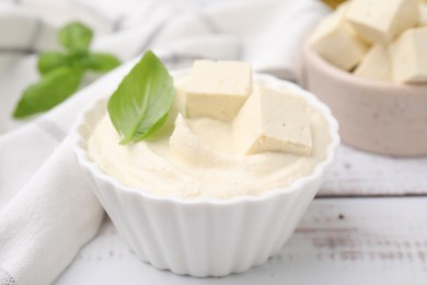 Photo of Delicious tofu sauce and basil leaf on white wooden table, closeup