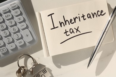 Photo of Notepad with phrase Inheritance Tax, calculator and keys with house shaped key chain on white table, flat lay