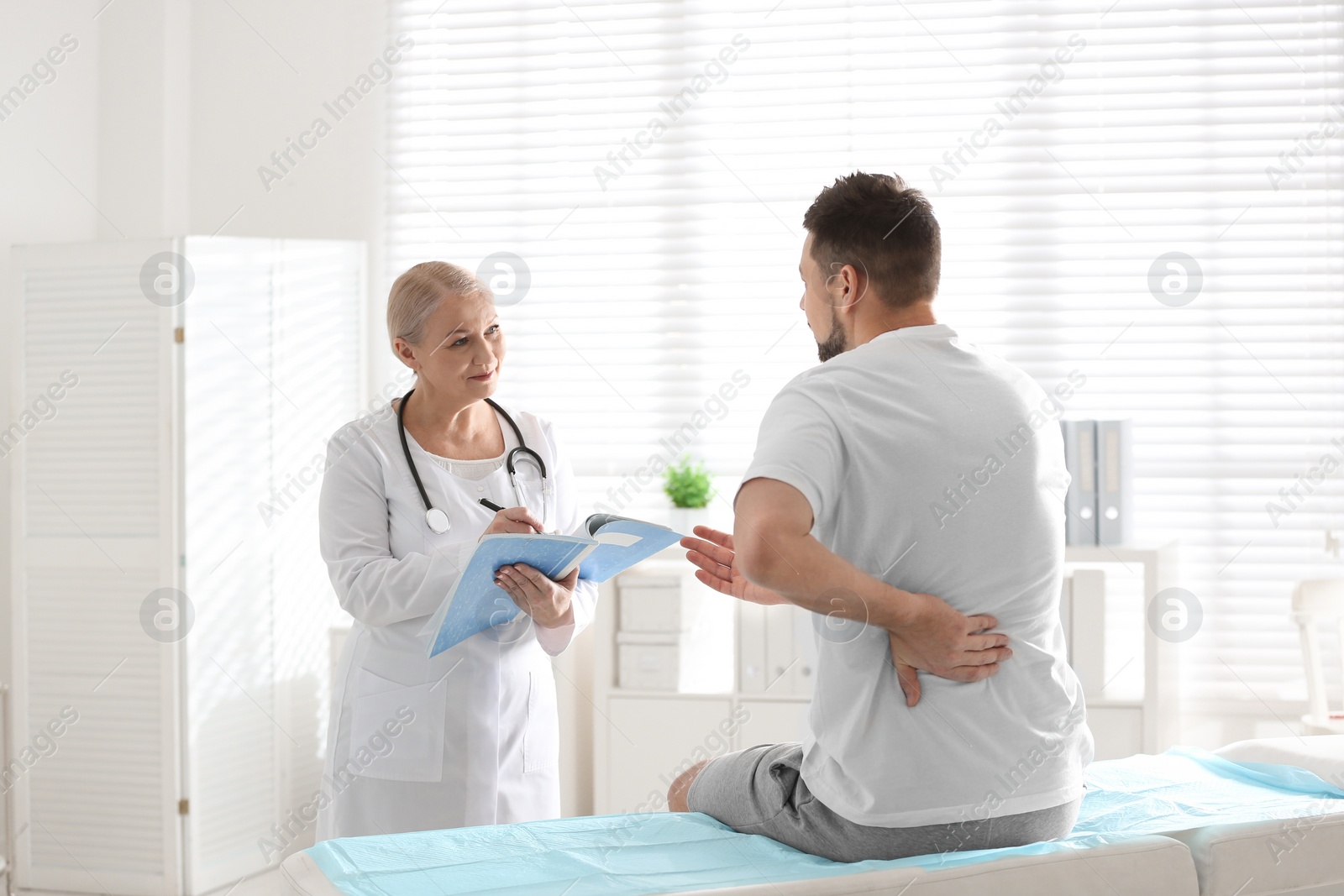 Photo of Female orthopedist examining patient with injured back in clinic