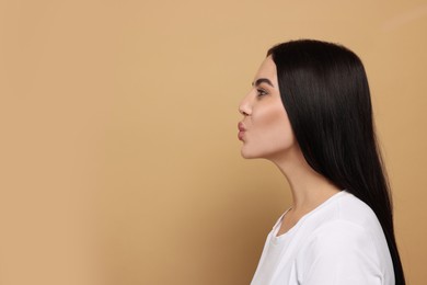 Photo of Beautiful young woman blowing kiss on beige background. Space for text