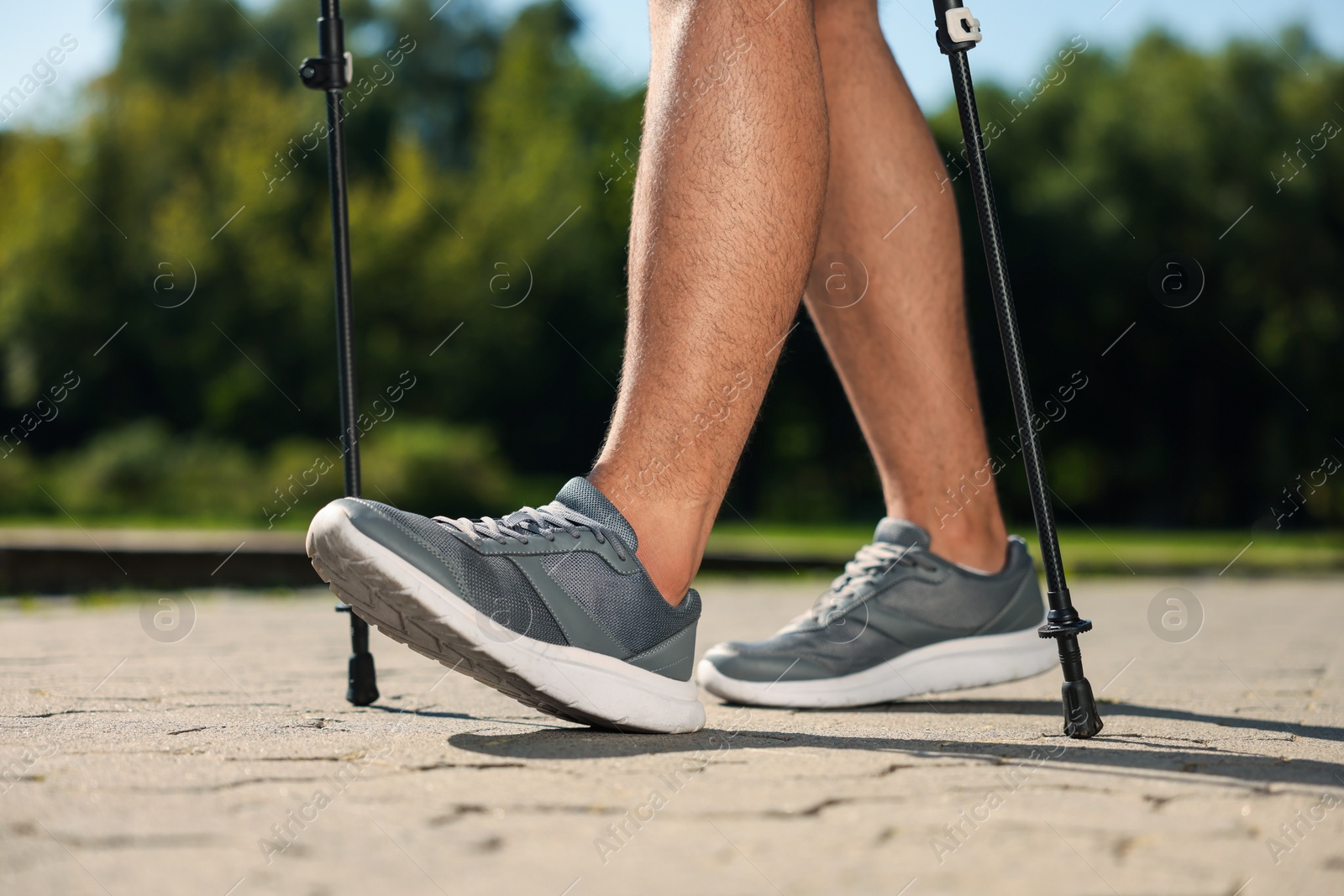 Photo of Man practicing Nordic walking with poles outdoors on sunny day, closeup