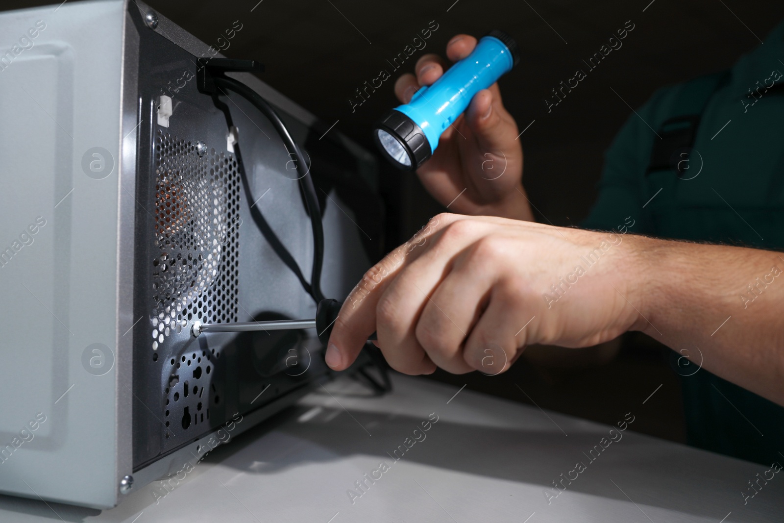 Photo of Repairman with flashlight fixing microwave oven indoors, closeup