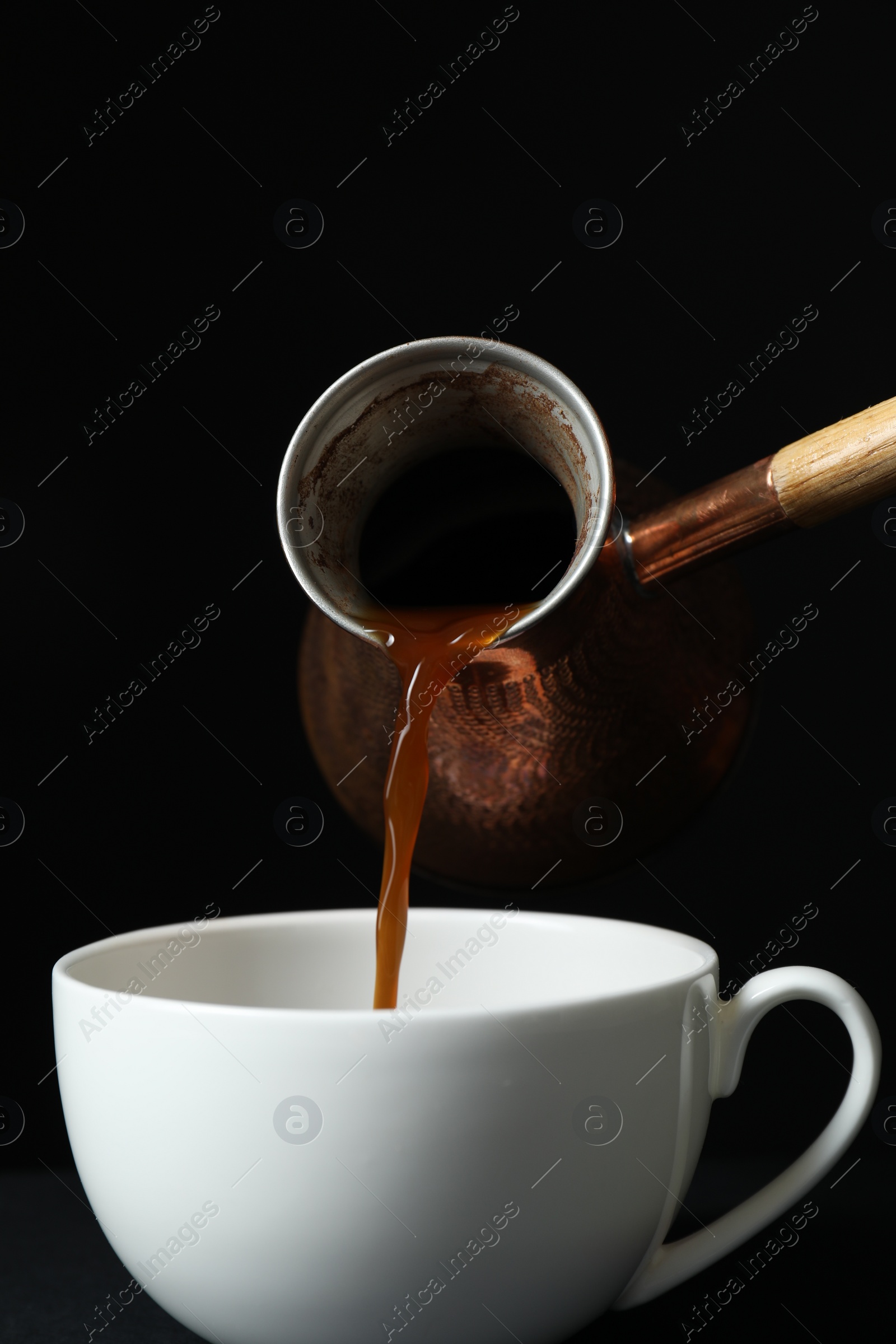 Photo of Turkish coffee. Pouring brewed beverage from cezve into cup against black background