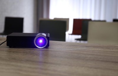 Modern video projector on wooden table in conference room. Space for text