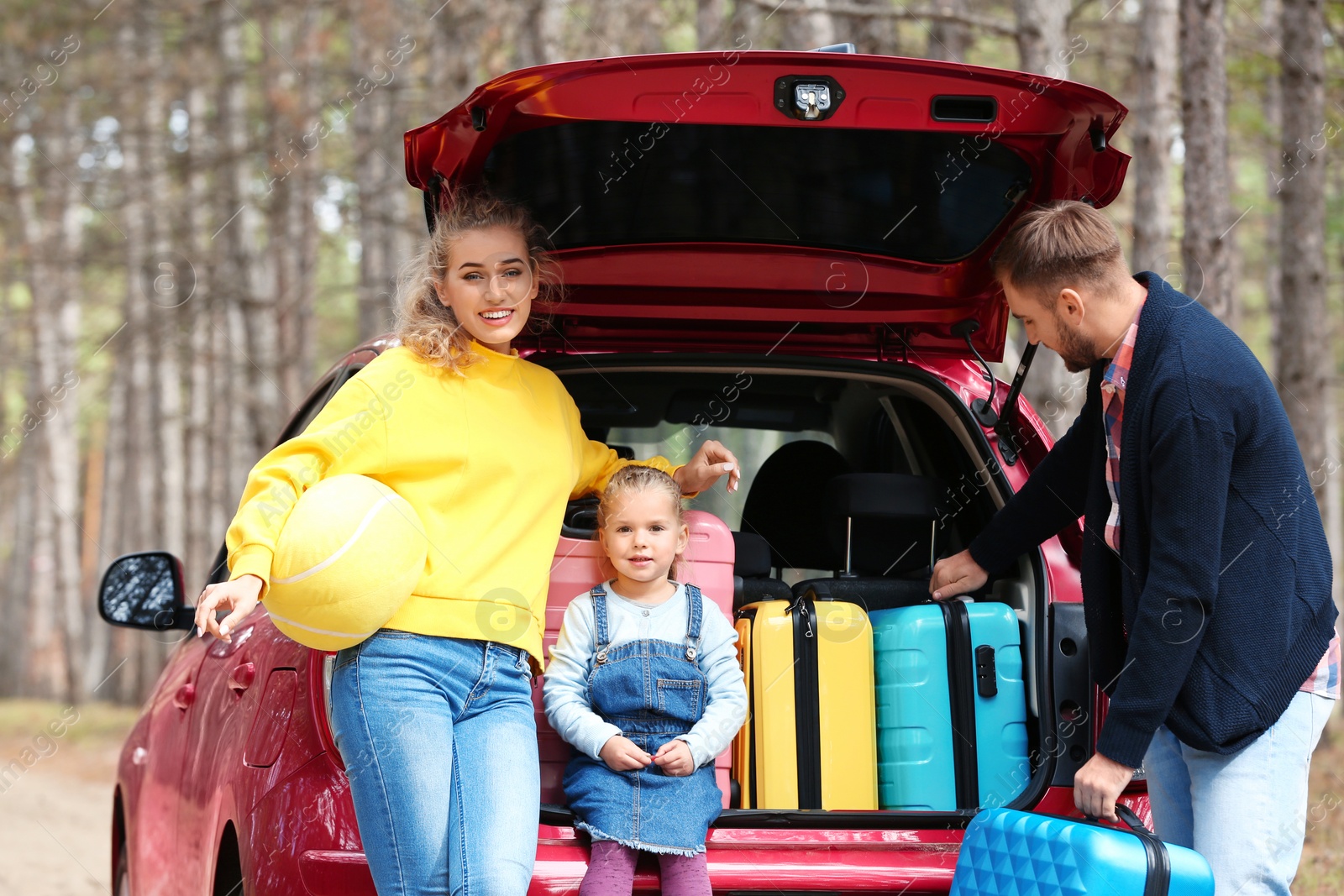 Photo of Happy young family near car trunk loaded with suitcases outdoors