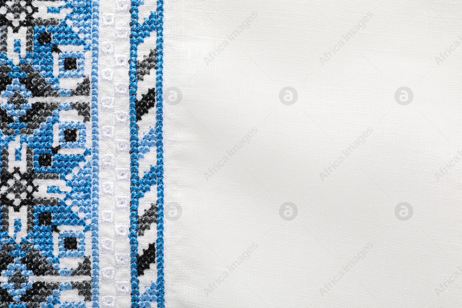 Photo of Beautiful light blue Ukrainian national embroidery on white fabric, top view. Space for text