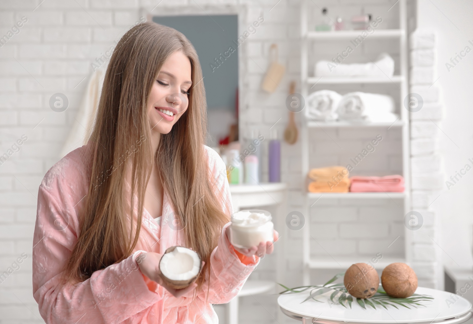 Photo of Young woman with coconut oil for hair in bathroom