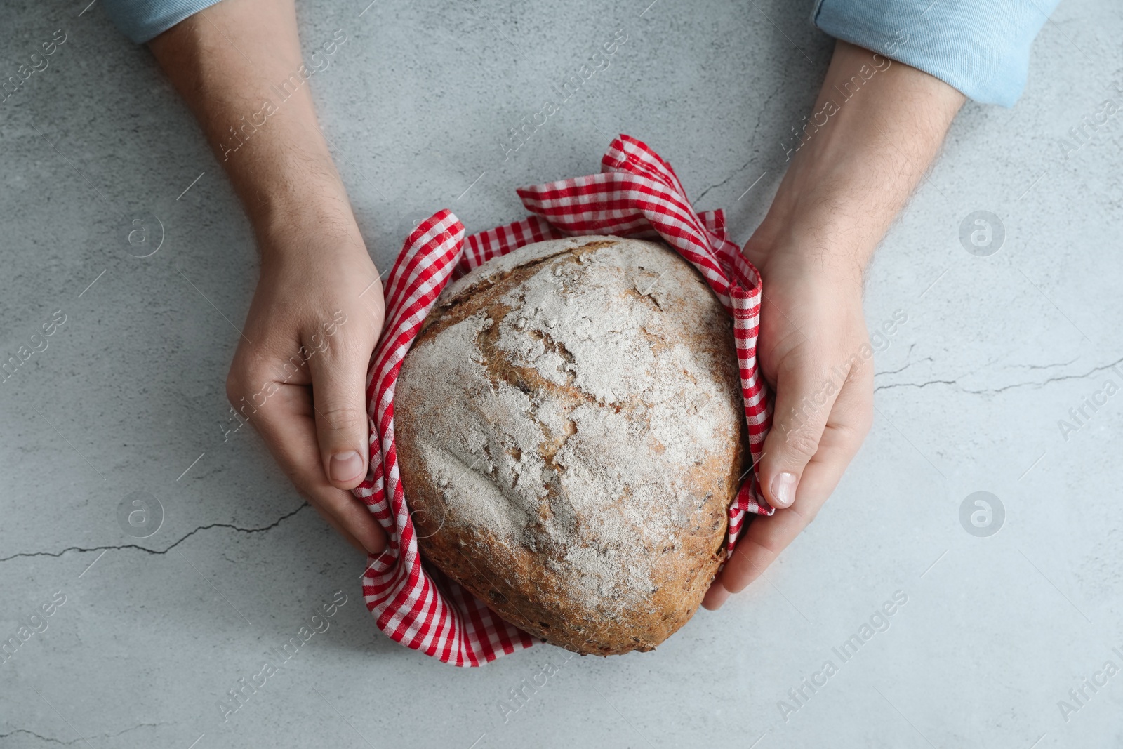 Photo of Man holding loaf of fresh bread at grey table, top view